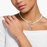 Woman wearing a pearl necklace with charms, ring, and bracelet on a white background