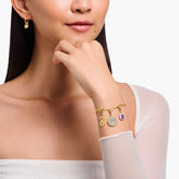 Woman wearing a gold bracelet with charms on a plain background
