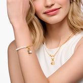 Woman wearing a gold necklace and bracelet with charms on a plain background