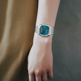 Wrist wearing a silver watch with a blue face