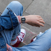 Person wearing a digital watch with jeans and red sneakers on a sidewalk.
