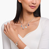 Woman wearing a silver necklace with charms, earrings, and bracelet on a white background