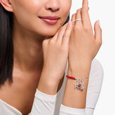 Woman wearing a silver bracelet with charms on her wrist, with a plain background