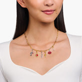 Woman wearing a gold necklace with various charms on a white background