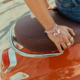Person sitting on a red scooter with brown seat, wearing multiple bracelets and rings.