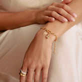 Gold bracelet with charms on a wrist against a neutral background