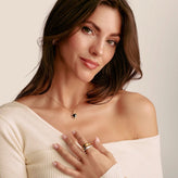Woman wearing a necklace with a heart pendant and rings on a plain background