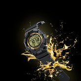A rugged digital sports watch with a black strap and case, featuring a gold-toned bezel and a yellow-green LCD display, shown with a dramatic gold splash effect against a black background.