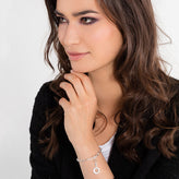 Woman wearing a silver bracelet with a circular charm on a plain background