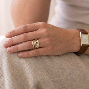 Hand wearing multiple gold rings on a neutral background